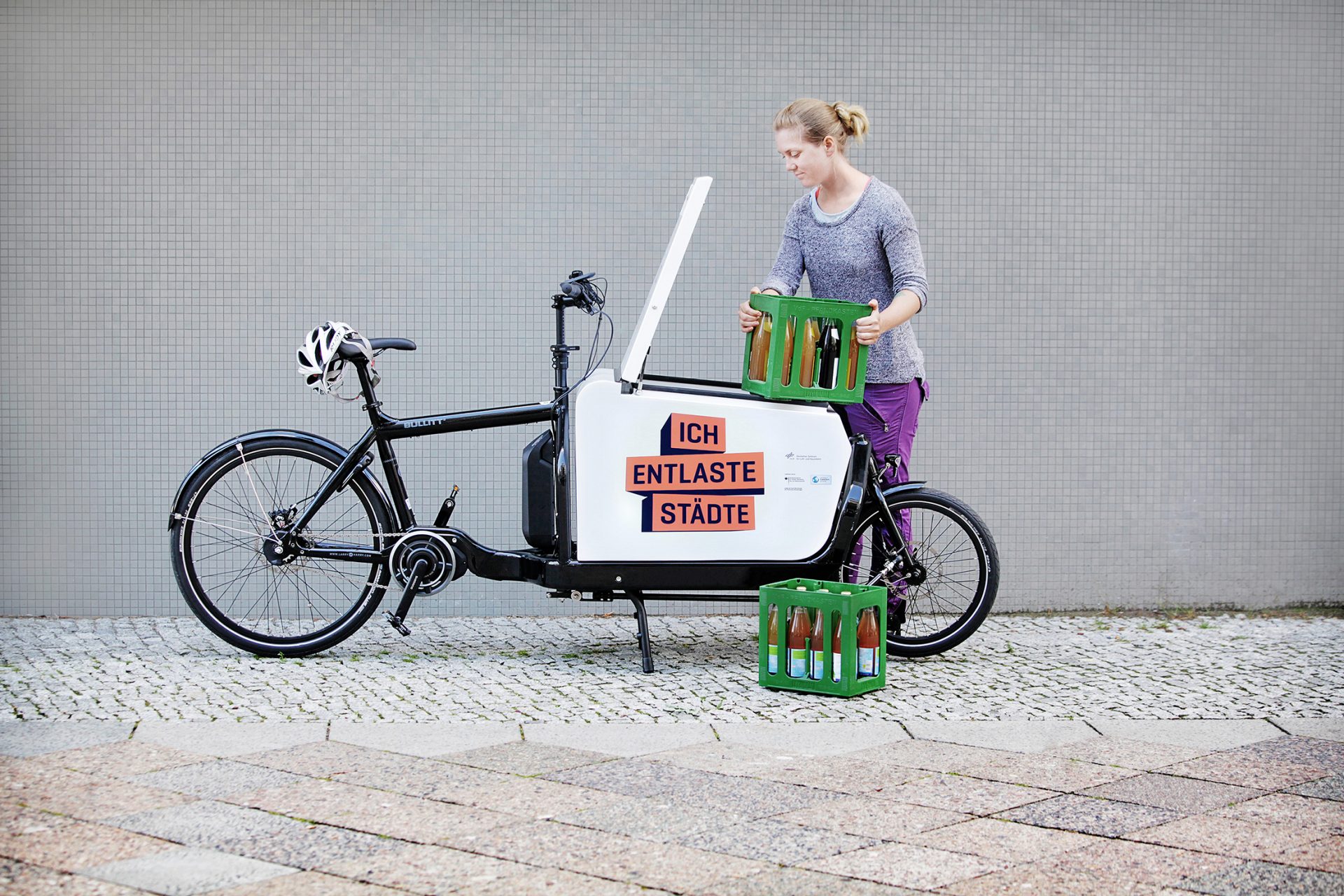 Une femme charge des caisses de boissons sur un vélo-cargo. Sur le vélo, il y a 